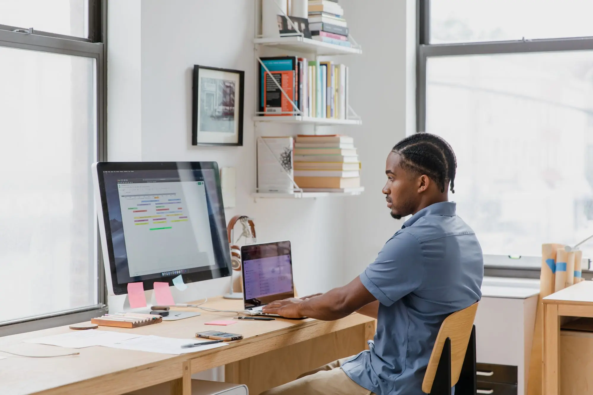 Business owner at a desk working across a desktop monitor and a laptop, checking accounts from an old and a new bank side by side