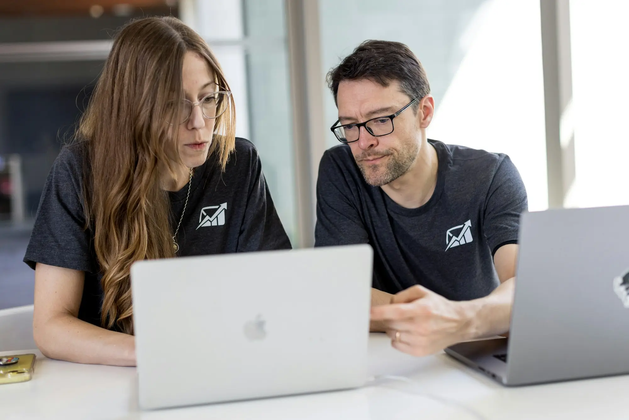 Two business co-directors at a shared desk checking open banking data-sharing settings on their laptops